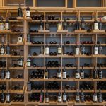 This commercial custom wine cellar has a tall, wall-mounted wooden wine shelf. There's a rolling library ladder attached to it to help people grab a bottle on top.