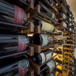 Matte black rods with dark stained wooden brackets hold the bottles in this modern wine closet design.